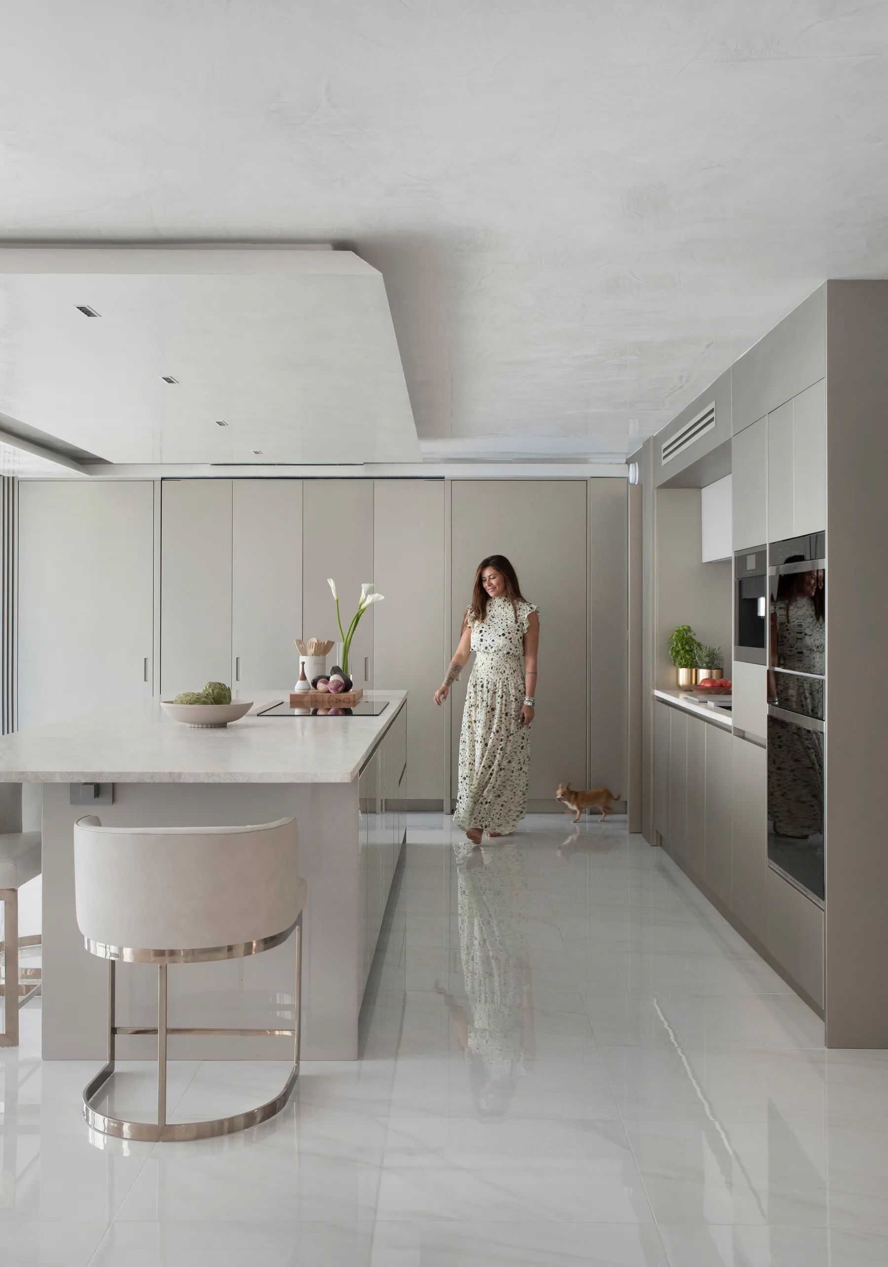 Woman walking through the white lacquer kitchen with waterfall island and polished marble floors in the Boca Raton high-rise residence