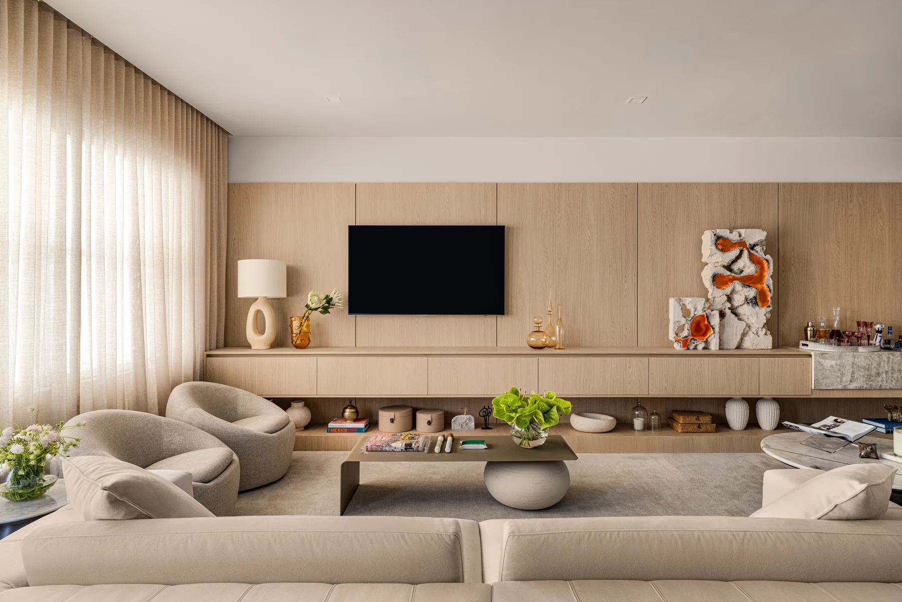 Oak-panelled living room with floating console, sculptural artwork and bouclé swivel chairs in the HOME A&A residence by Paula Ambrosio Interiors